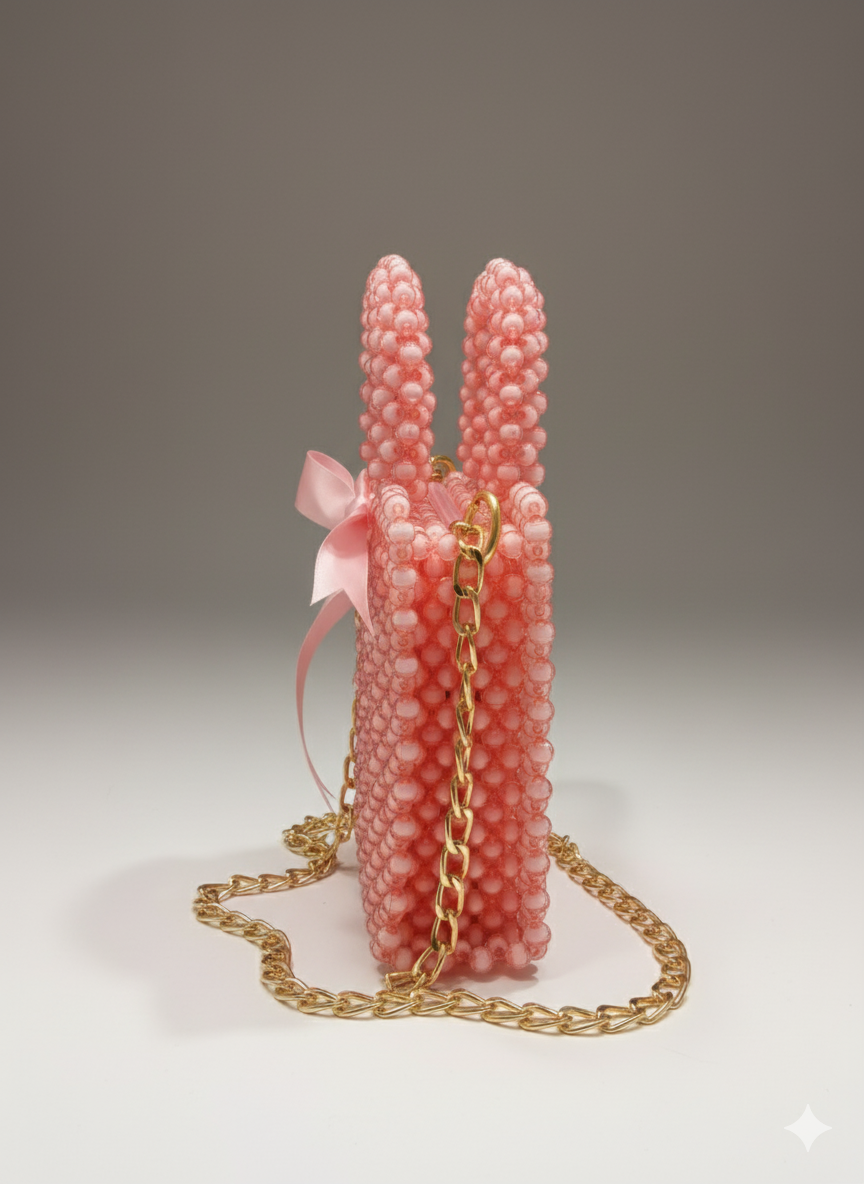 unique, vertical pink beaded mini-bag shaped like a bunny, complete with two long ear-like handles, a small pink ribbon, and a gold chain crossbody strap.